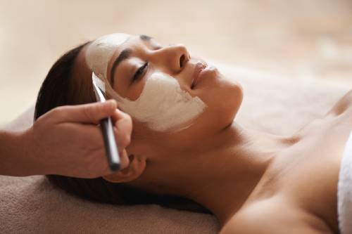 Your skin deserves some pampering. A face mask being applied to a beautiful young woman at a beauty spa.