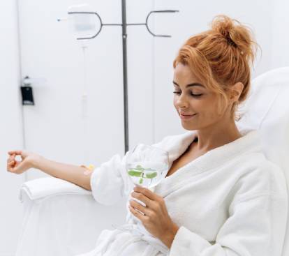 Woman in white bathrobe sitting in armchair and receiving IV infusion