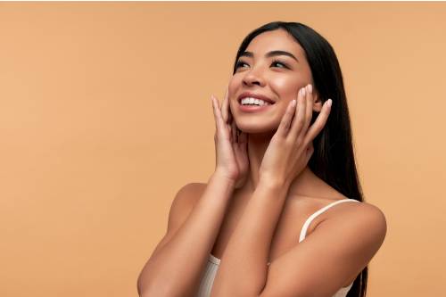 Young Asian woman with clean healthy glowing skin in white top isolated on beige background. Facial skin care concept, spa, cosmetology, plastic surgery.