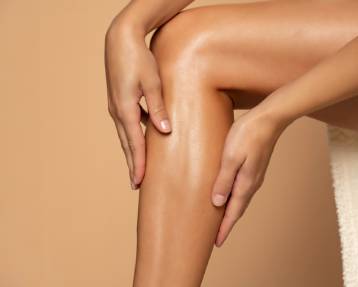 Close-up on a woman applying cream on her legs on beige background